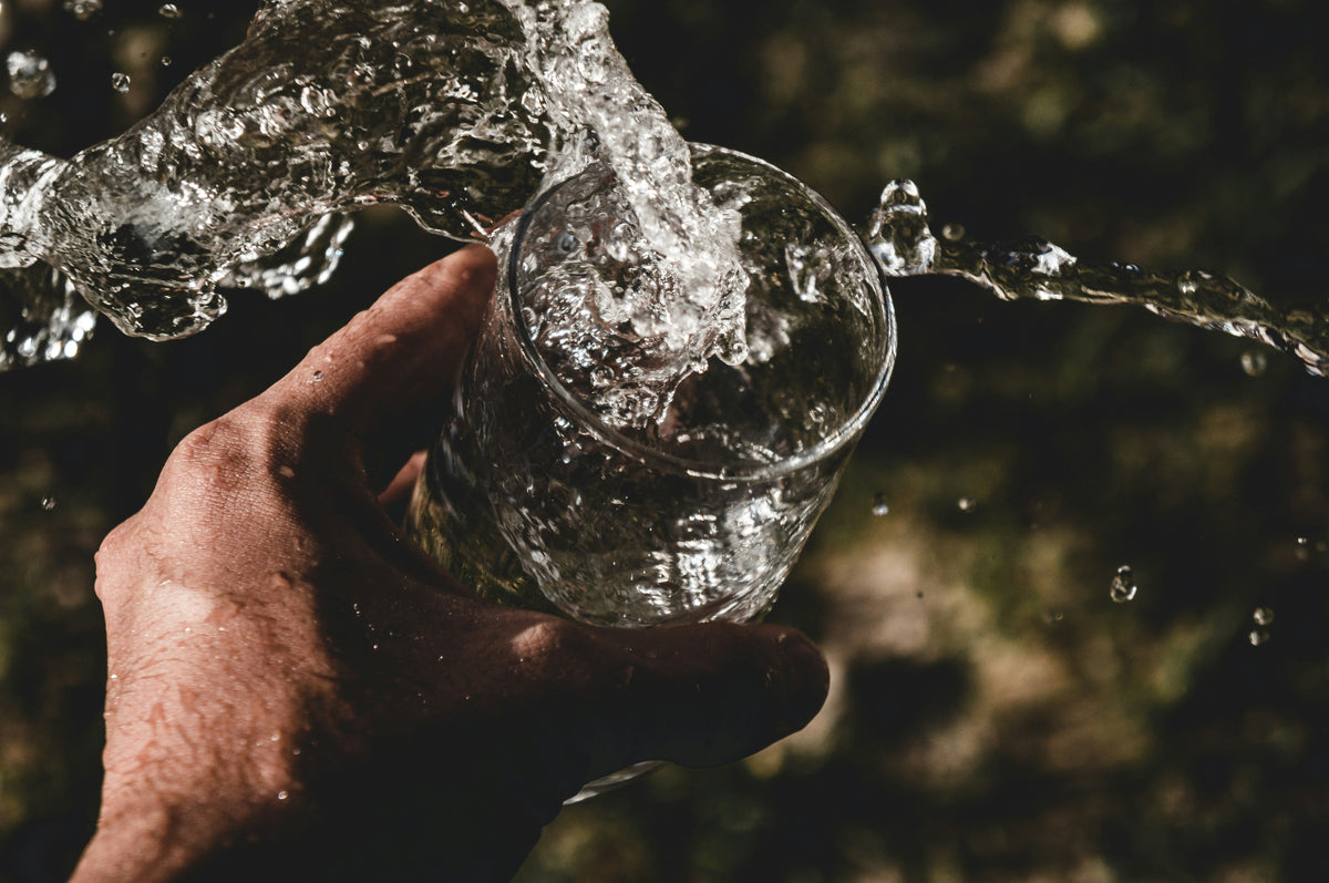 Water splashing out of a glass held in one hand, illustrating water loading and fluid manipulation in sports nutrition.