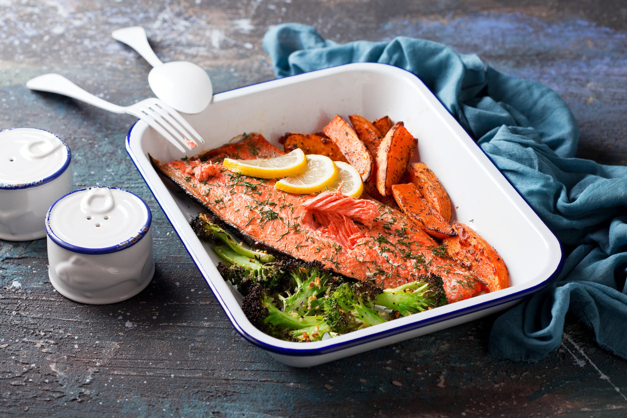 Healthy meal of baked salmon with sweet potato wedges and broccoli in a white dish.