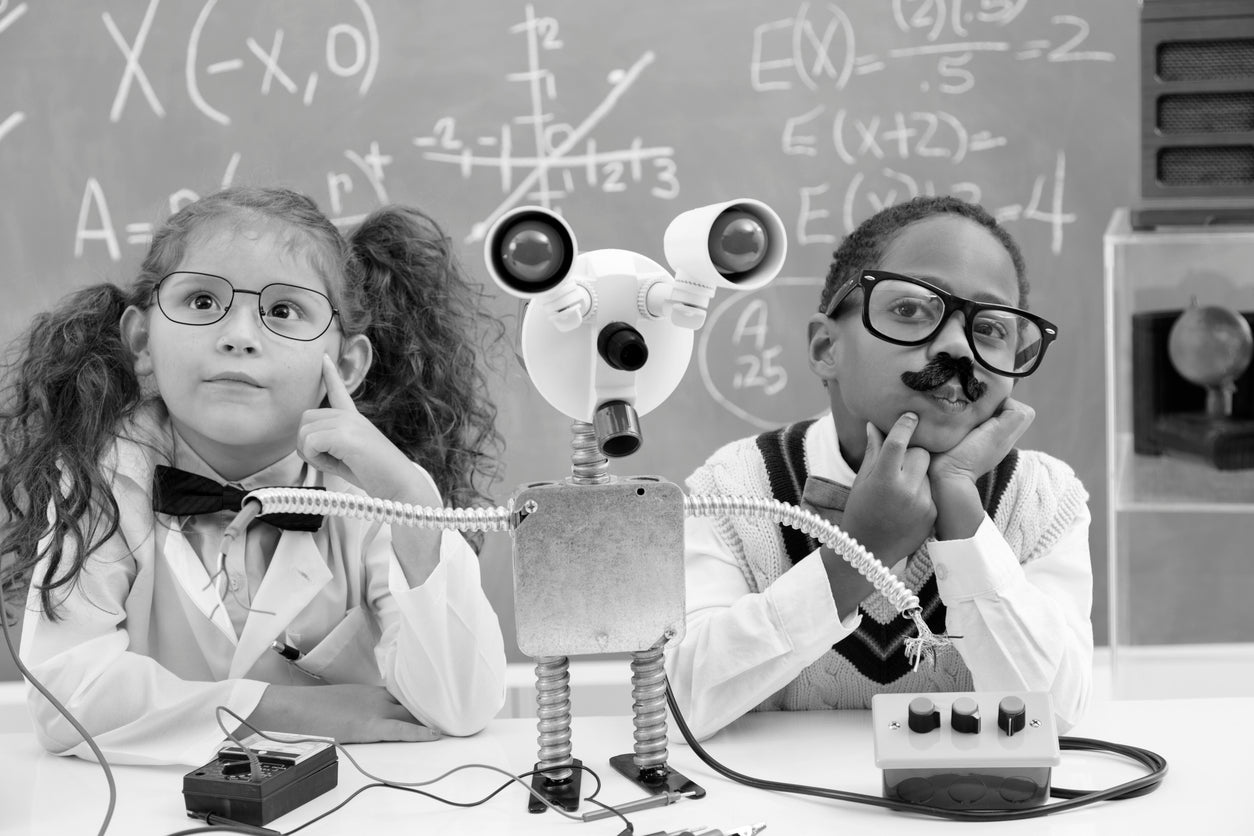 Children dressed as young scientists with a homemade robot and equations on the chalkboard behind them.