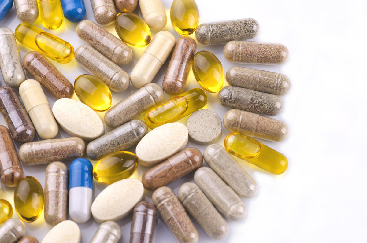 Mix of dietary supplement capsules and softgel tablets on a clean white surface.