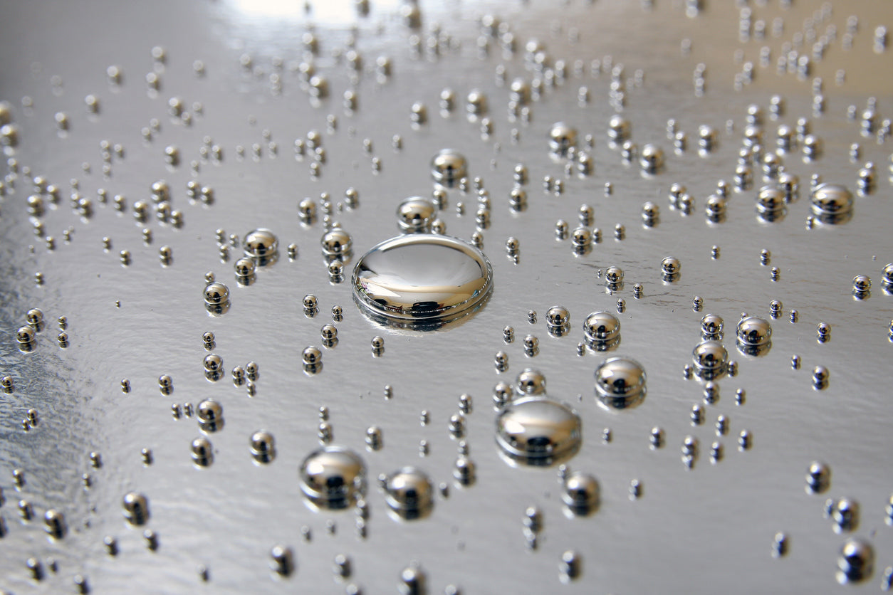 Close-up of shiny metallic droplets on a reflective surface, representing heavy metals.
