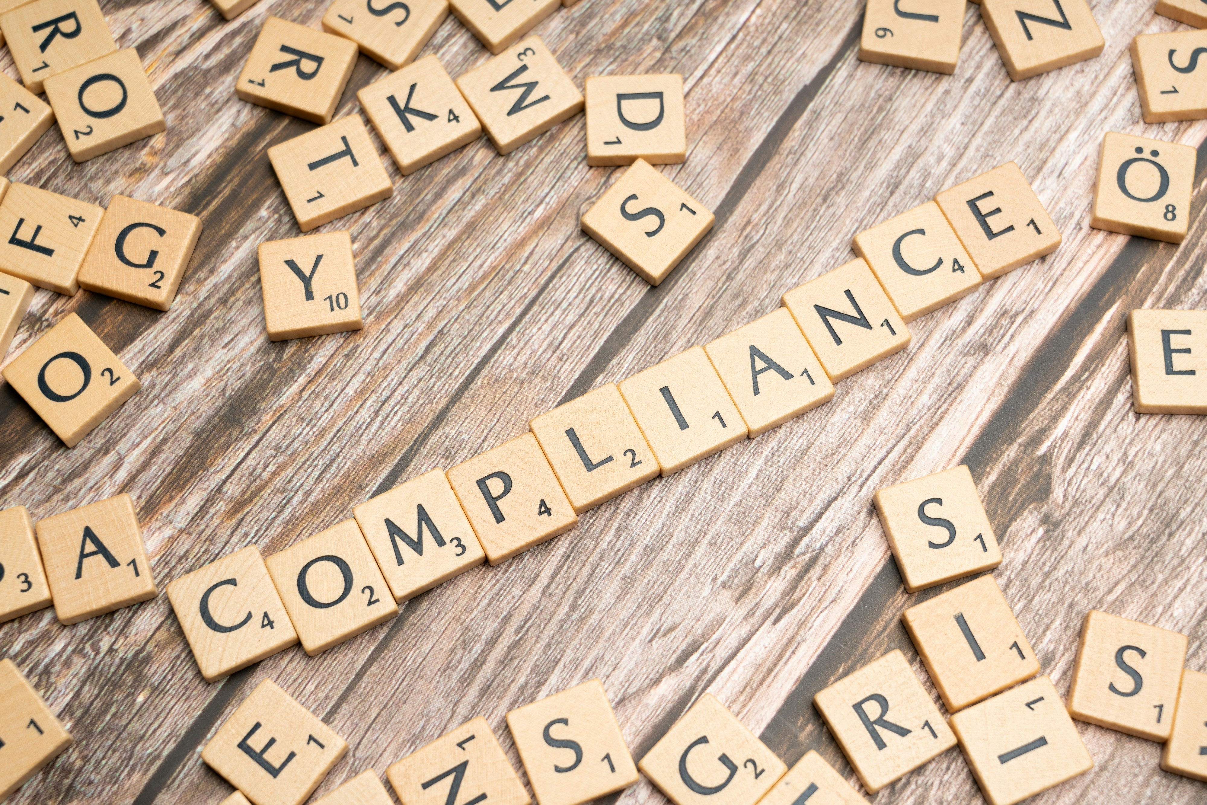 Wooden letter tiles spelling “compliance” on a wooden desk