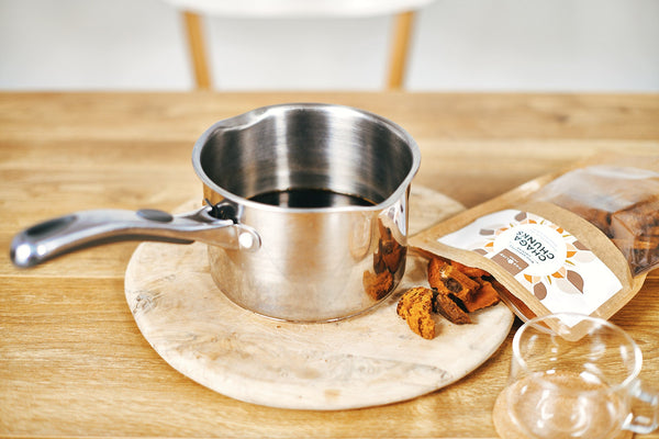 One Life Foods Chaga mushroom pieces beside a pan of brewing Chaga tea.