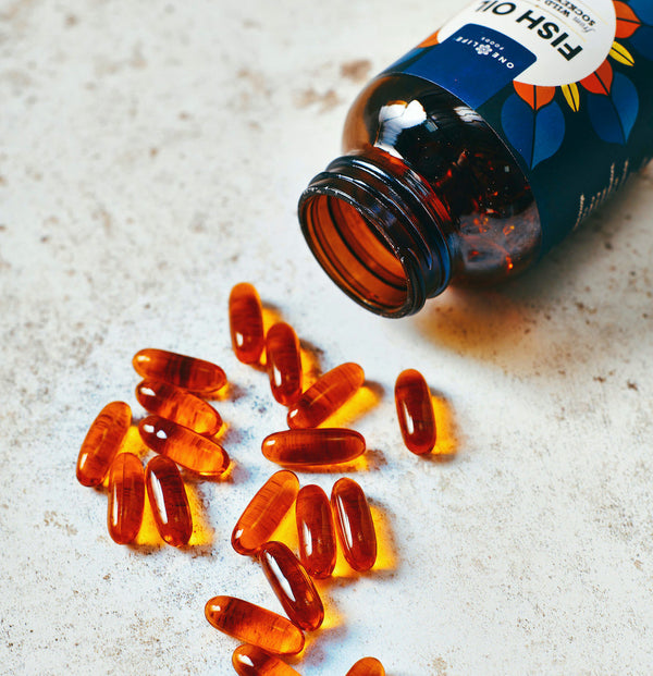 Bottle of fish oil capsules from One Life Foods with softgels spilled on a light surface.