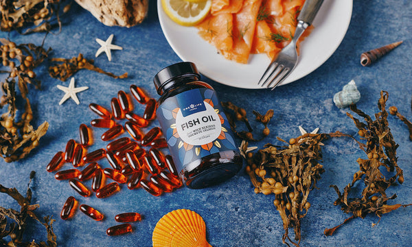 Bottle of One Life Foods fish oil capsules on a blue surface with seaweed and a plate of salmon.