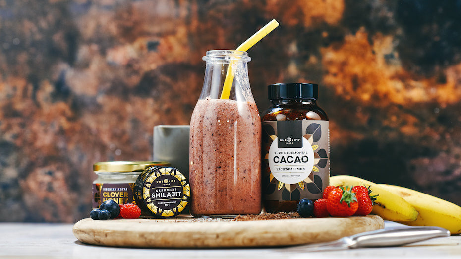 One Life Foods cacao blend, Shilajit resin, and honey displayed beside a berry smoothie.