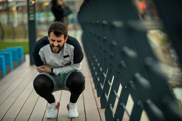 Male athlete crouching outdoors and holding his stomach, representing gut discomfort.