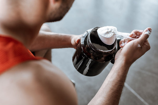 Person scooping white pre-workout from a black container before mixing a supplement drink.