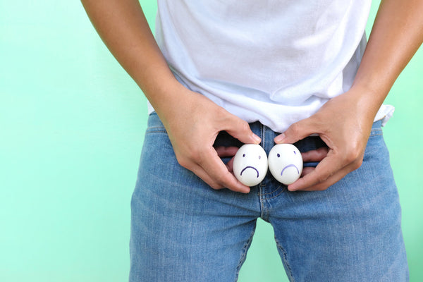 Person holding two eggs with sad faces drawn on them as a humorous metaphor for male reproductive health.