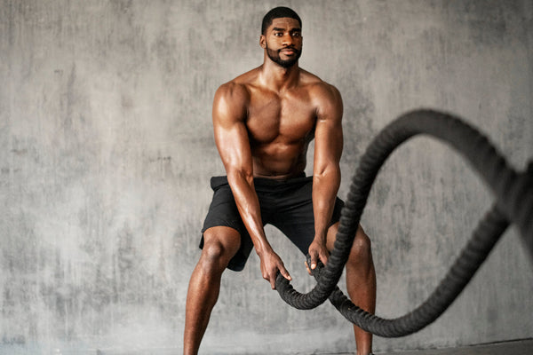 Male athlete training with battle ropes in a gym, showing strength and endurance.