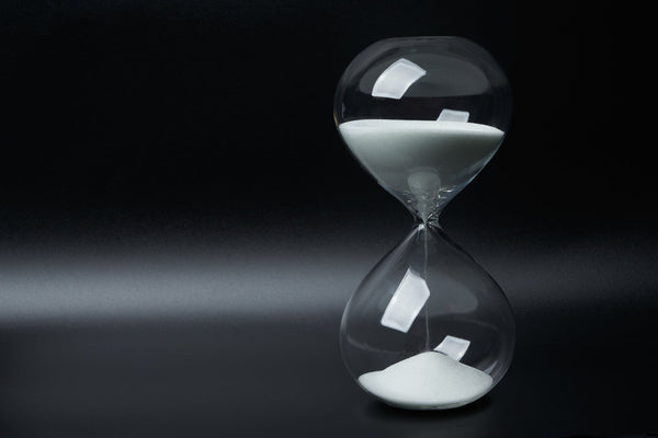 Clear glass hourglass with white sand falling slowly against a dark background, symbolising the time supplements take to work.
