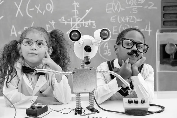 Children dressed as young scientists with a homemade robot and equations on the chalkboard behind them.