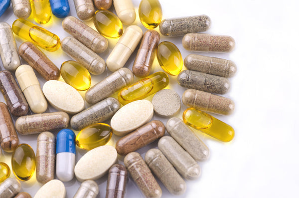 Mix of dietary supplement capsules and softgel tablets on a clean white surface.