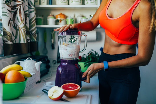 Athletic woman making a healthy smoothie with fresh fruit in a kitchen.