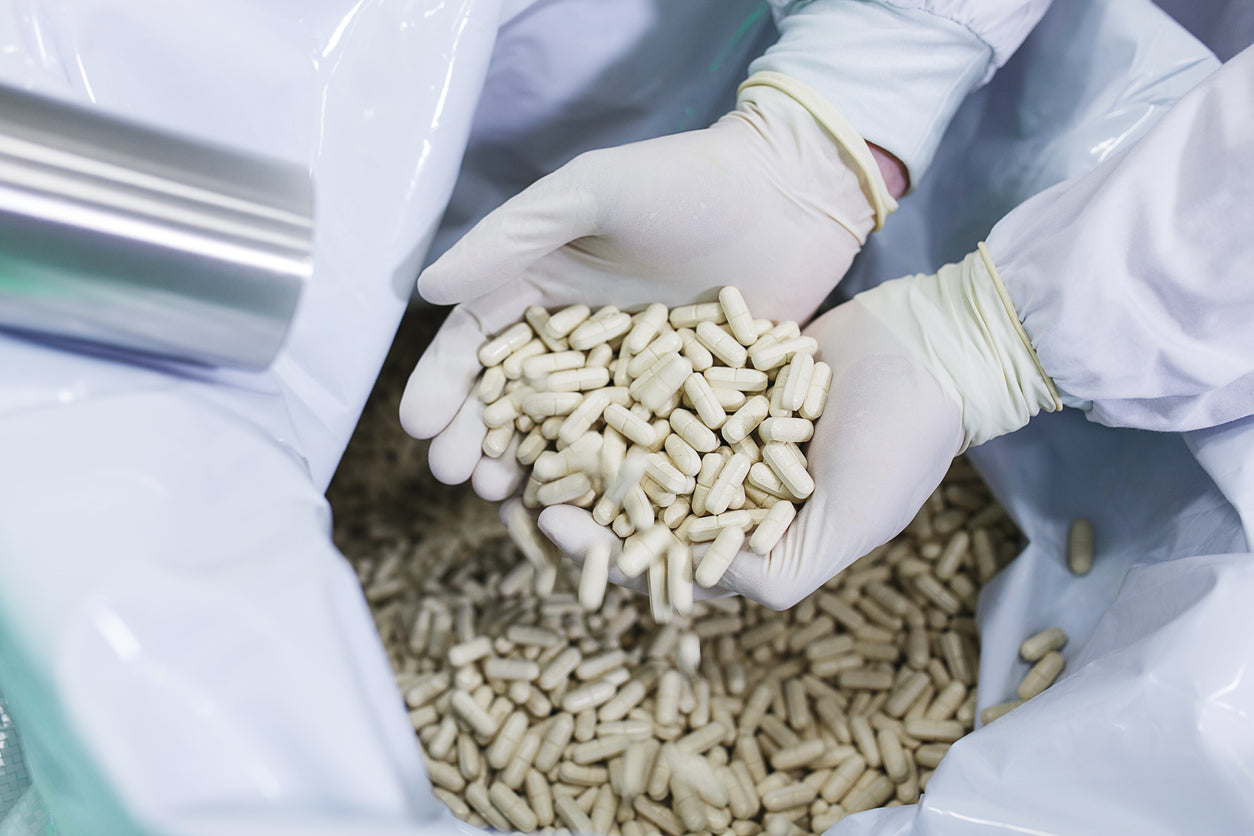Gloved technician inspecting supplement capsules during production, symbolising quality control and supplier transparency.
