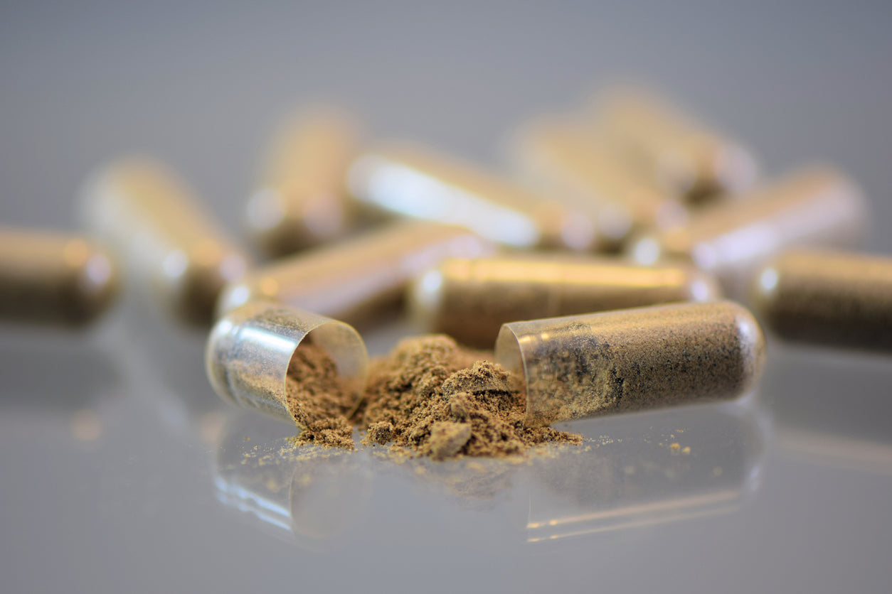 Open supplement capsules with herbal powder on a reflective surface.