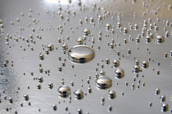 Close-up of shiny metallic droplets on a reflective surface, representing heavy metals.