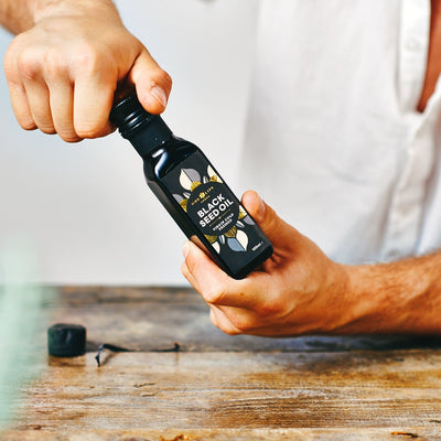 Opening bottle of black seed oil cold pressed Nigella sativa supplement