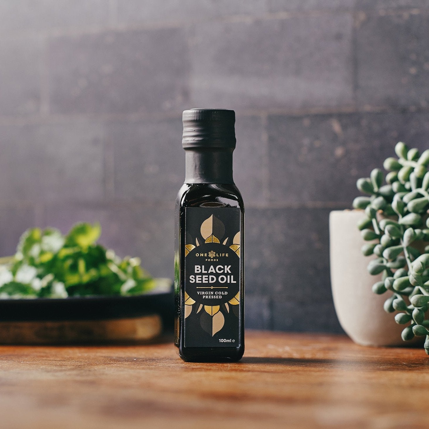 Black seed oil bottle in natural setting with plants and wooden surface