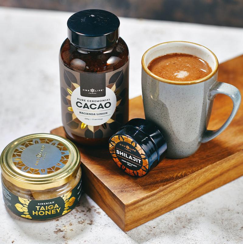 Ceremonial cacao drink with mug, cacao jar, shilajit and honey on wooden board