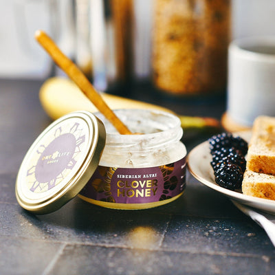 Siberian Altai clover honey with wooden honey dipper in open glass jar