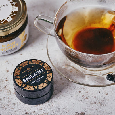One Life Foods shilajit resin beside a glass of tea and raw honey.