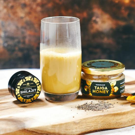 Glass of turmeric milk with honey and shilajit on wooden surface